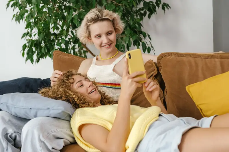 Deux colocataires détendues sur un canapé regardent ensemble un téléphone.