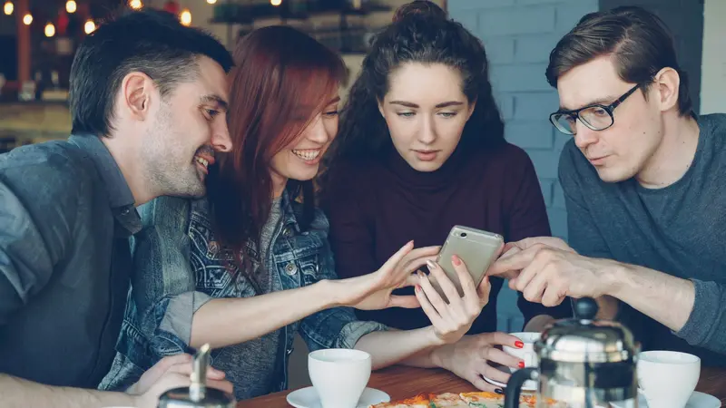 Quatre amis attablés dans un café se penchent sur le même téléphone.
